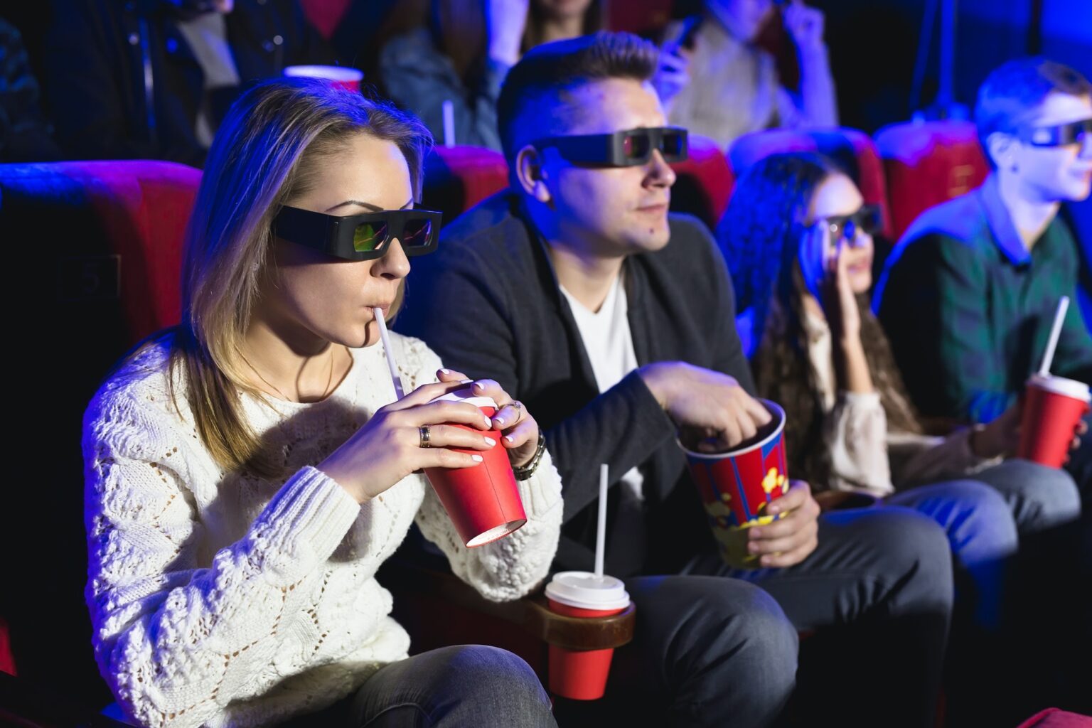 Happy couple sitting in movie theater, watching 3D movie, eating popcorn